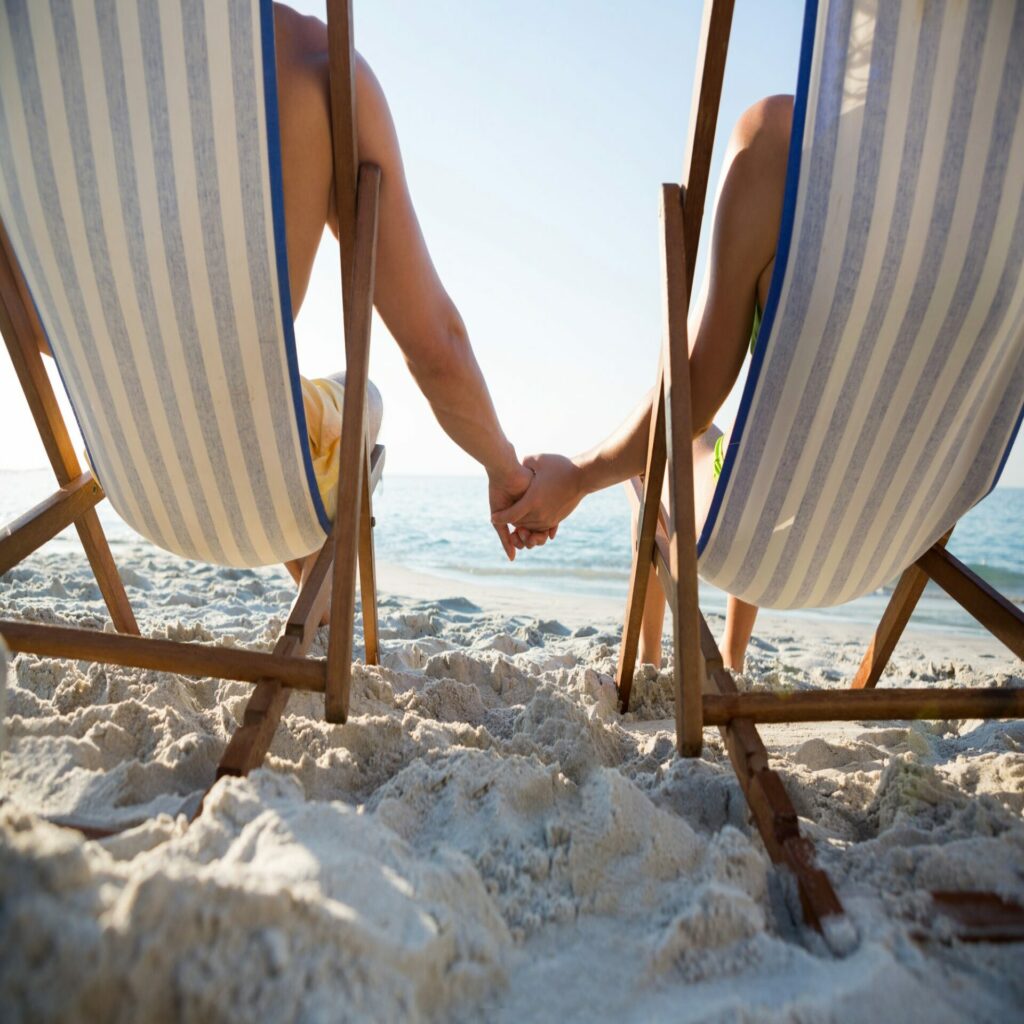 Couple holding hands while relaxing on lounge chairs at beach