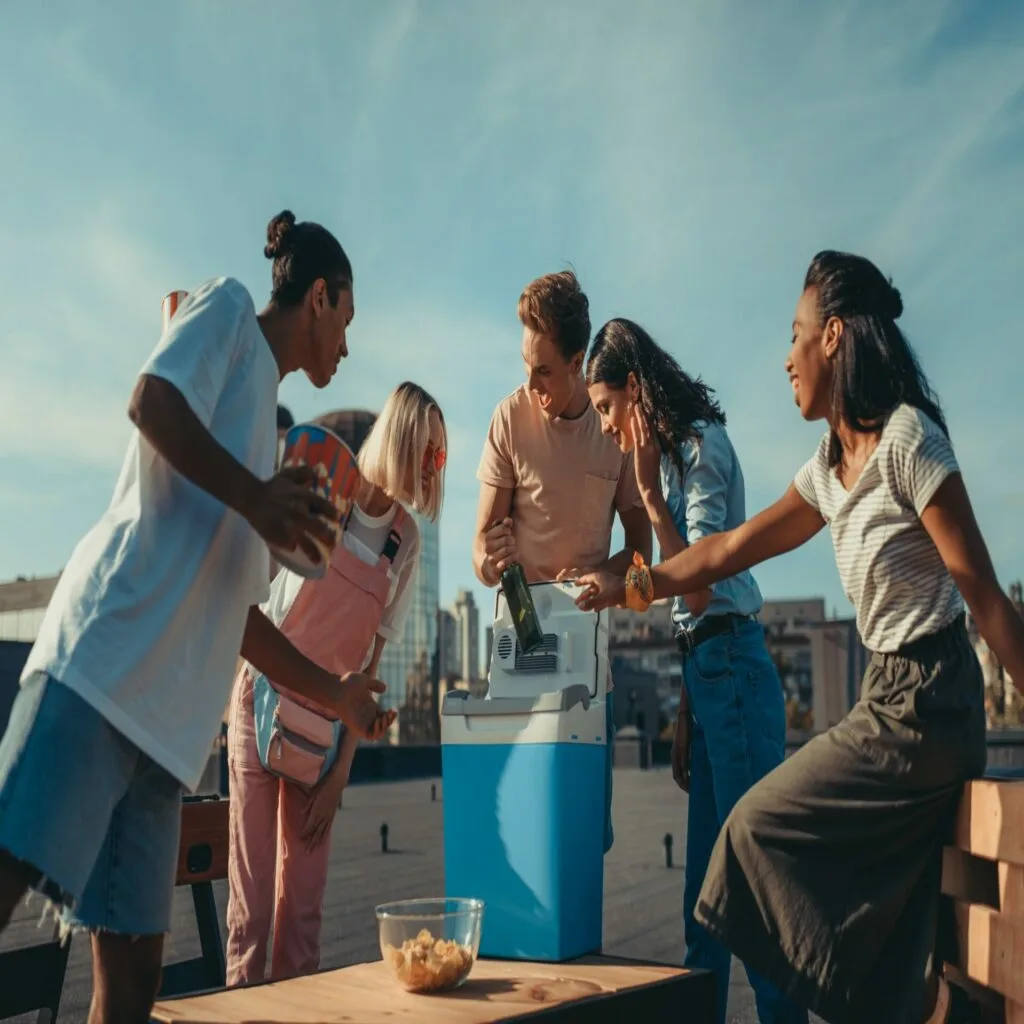 group of happy excited friends with fridge container of beer on roof