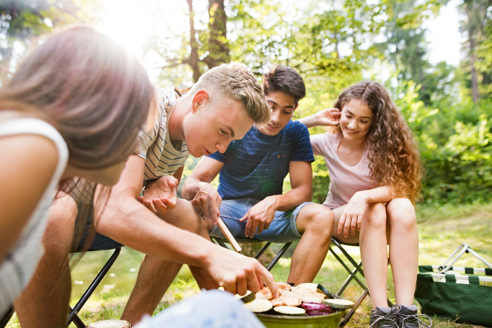 Teenagers camping, cooking vegetables on barbecue grill.