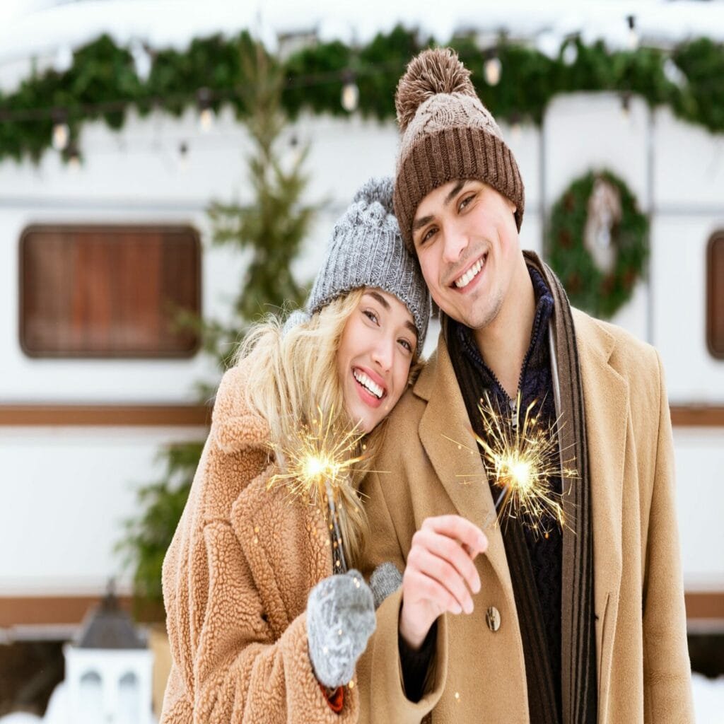 Smiling Romantic Couple In Knitted Hats Posing With Sparklers At Winter Camping