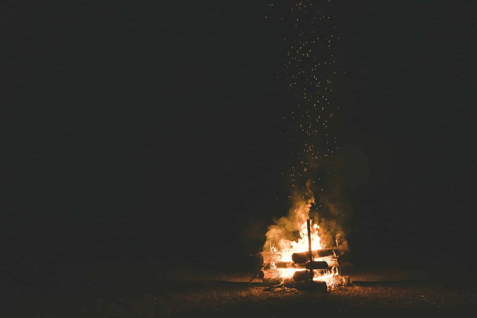 A campfire with sparks flying around in the dark night