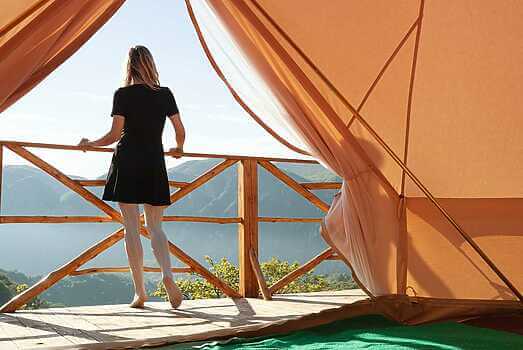 young woman watching the mountains in front of a glamping tent