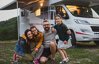 Happy family looking at camera outdoors at dusk, caravan holiday trip