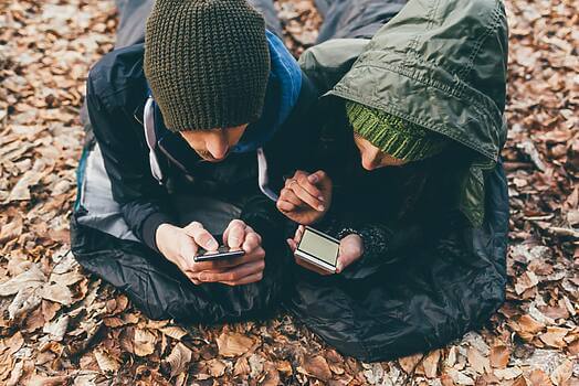 Hiking couple lying in sleeping bags looking at smartphones in forest, Monte San Primo, Italy