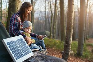 Little boy looks at camera lovely smile while sitting with a female near solar panel in forest