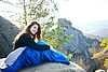 Woman sitting alone in sleeping bag on big mountain rock and smiling