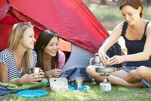 Three Young Women Cooking On Camping Stove Outside Tent