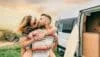 Couple kissing piggybacking next to their camper van during a trip