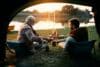Senior fisherman and his son having a drink while camping by the water at sunset.