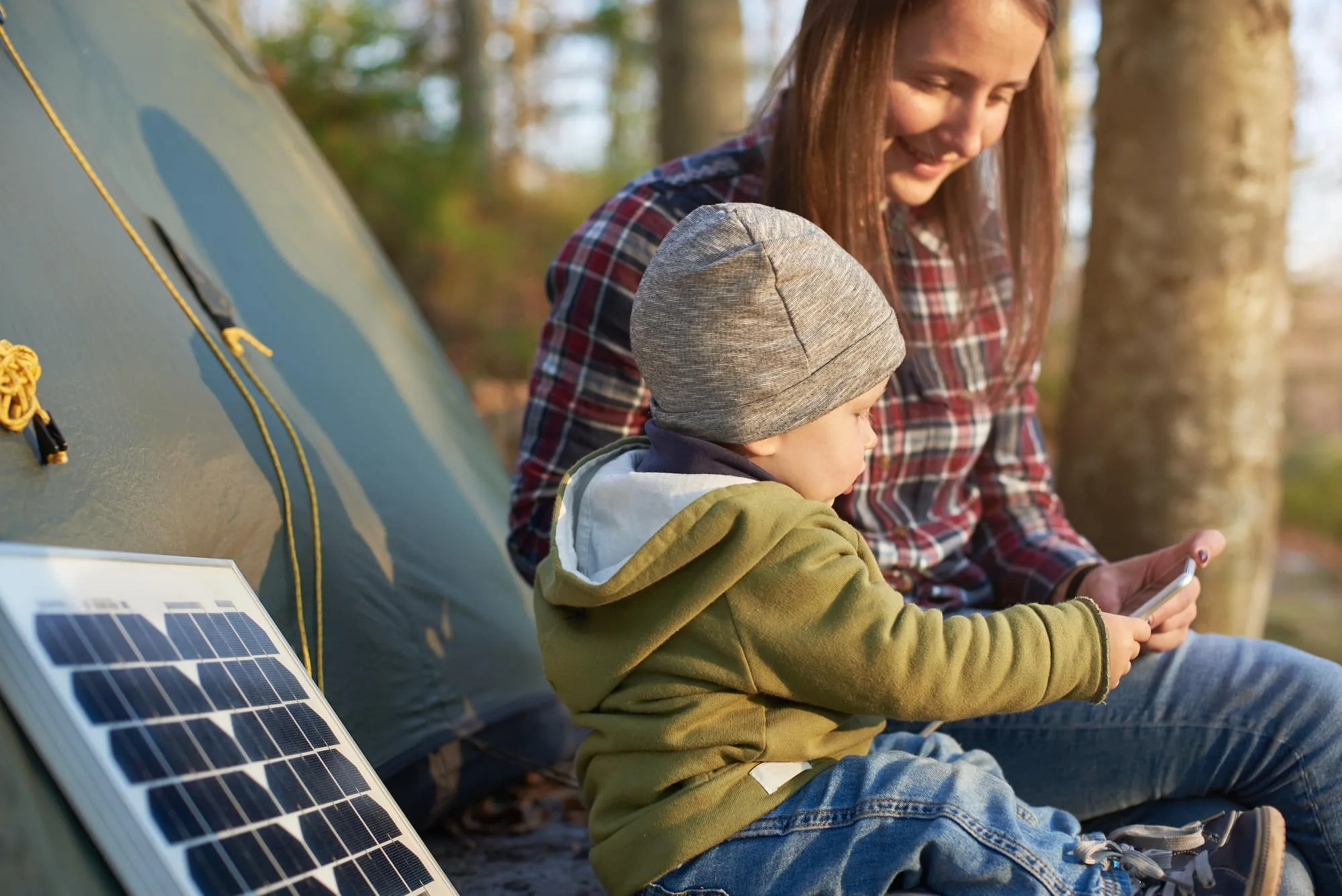 Campingabenteuer pur: Ihr ultimativer Guide für einen unvergesslichen Campingurlaub 9 Little wonderful kid takes the phone from girl sitting near solar panel at campsite in forest