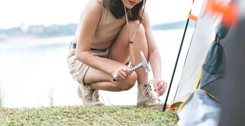 Familienfreundlich Unterwegs: Ihr Ultimativer Leitfaden für Familienzelte für den Campingurlaub 38 Young woman sticks a metal tent peg into the ground. Setting up a tent for camping.