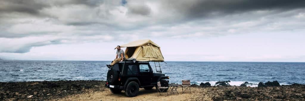 Das beste Jeep Wrangler Dachzelt für unvergessliche Abenteuer! 4 Banner travel header with man sitting on the roof of the car with camping tent having relax