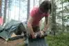 Woman tourist rolls up a hiking mat, against the background of a tent, in a camp