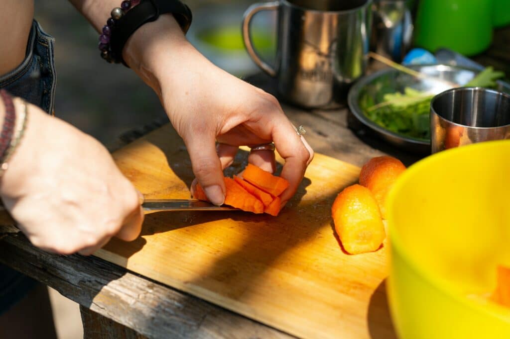 Hands slicing carrots into bars, outdoors, camping cooking