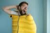 Man climbed into a yellow sleeping bag while standing indoors against a wall, imagining himself