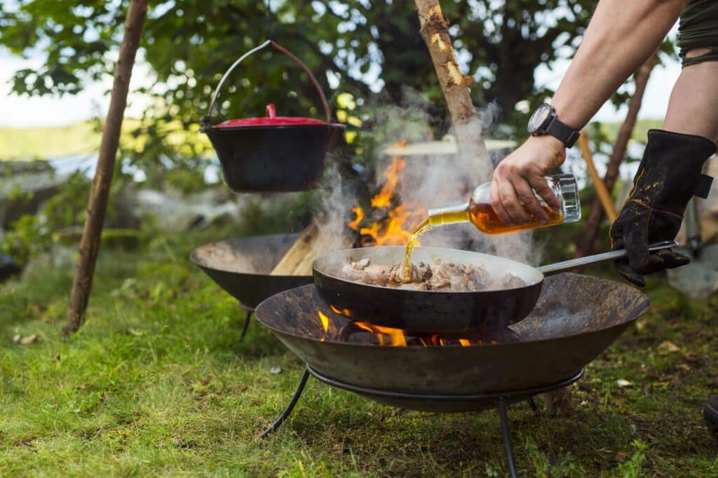 Man pouring alcohol on meat cooking over campfire