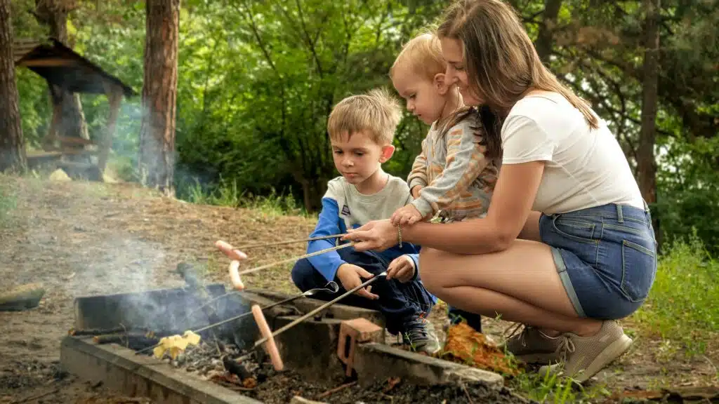 Camping Rezepte Familie: Einfache und leckere Gerichte für die ganze Familie 22 Young mother with two sons cooking sausages on bonfire in camp. Active leisure, children in camping