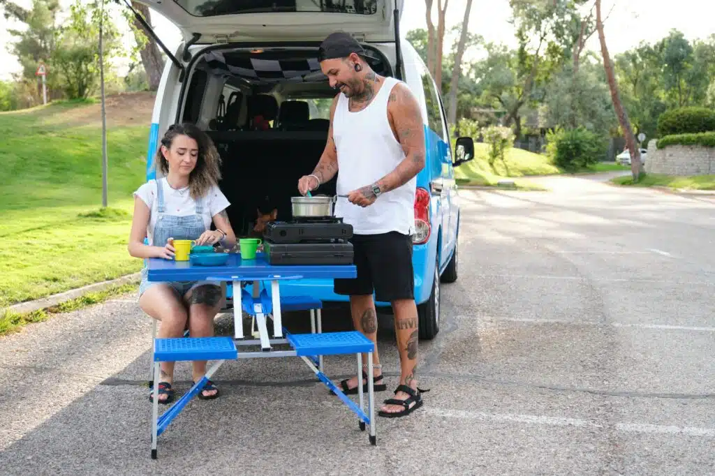 Camping Rezepte Familie: Einfache und leckere Gerichte für die ganze Familie 24 Young tattooed couple cooking in a camping gas kitchen near by the van.