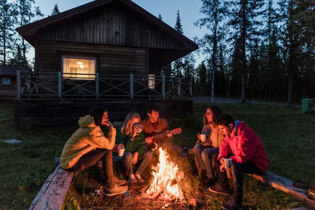 Campingurlaub in Schweden: Naturschönheiten und Outdoor-Erlebnisse entdecken 3 Group of friends sitting at a campfire, talking and playing guitar