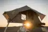 Car rooftop tent for camping on the roof rack of an off-road car in a desert at sunset