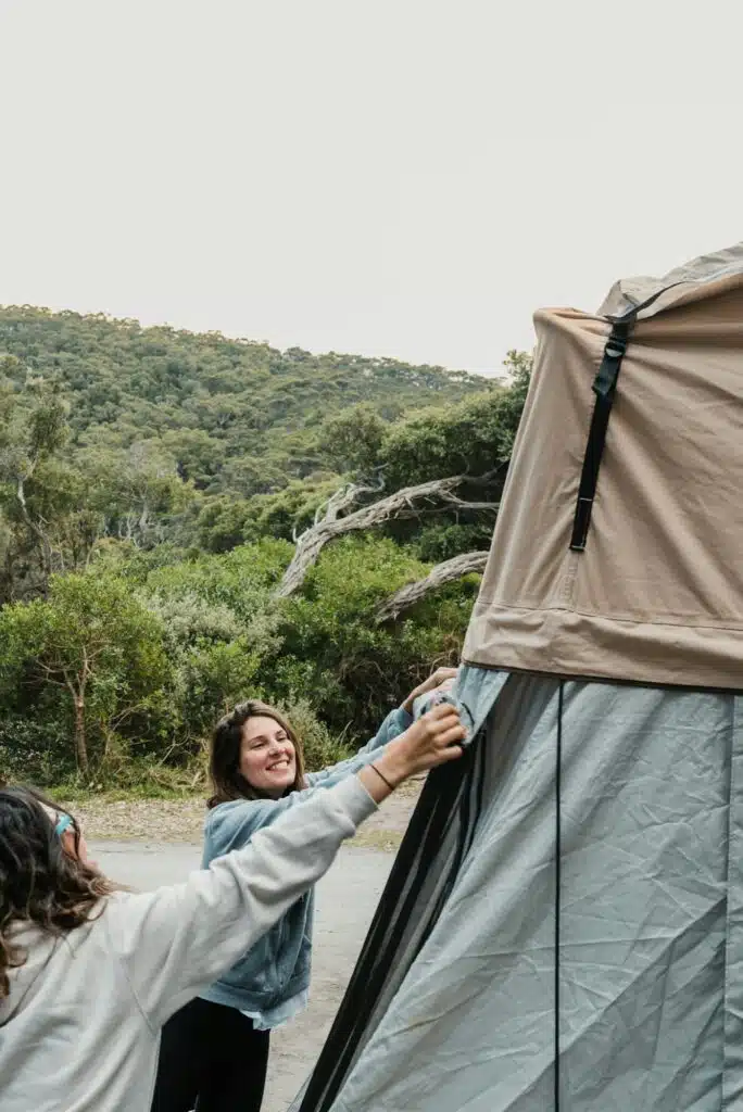 Two happy female backpackers set up a roof top tent in their 4WD