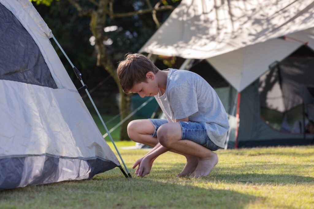 Schnellaufbau Zelt gesucht? So findest du dein Traumzelt für entspannte Campingmomente 1 A young boy secures a tent at a campsite, surrounded by other tents in a grassy area.