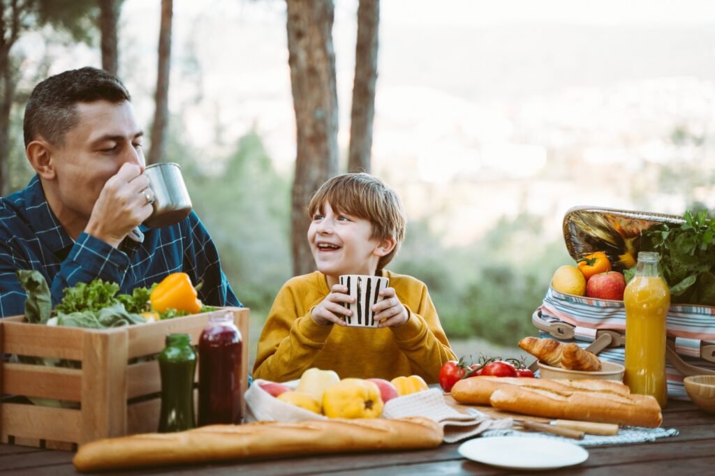 Veganes Campen für Einsteiger: Einfache Rezepte und praktische Tipps für die Outdoor-Küche 1 Father dad and school kid boy child having a picnic in the forest camping site with vegetables