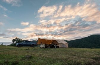 Group of friends relaxing inside large tent and pickup parked on hill in countryside at evening