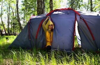 a girl in a yellow raincoat sets up a blue tent for camping in the forest, living in nature, prepari