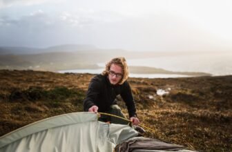 A man feeding a tent pole into the tent fabric in open space.