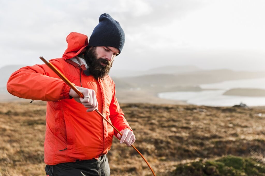 A man in an open landscape, holding a tent pole.
