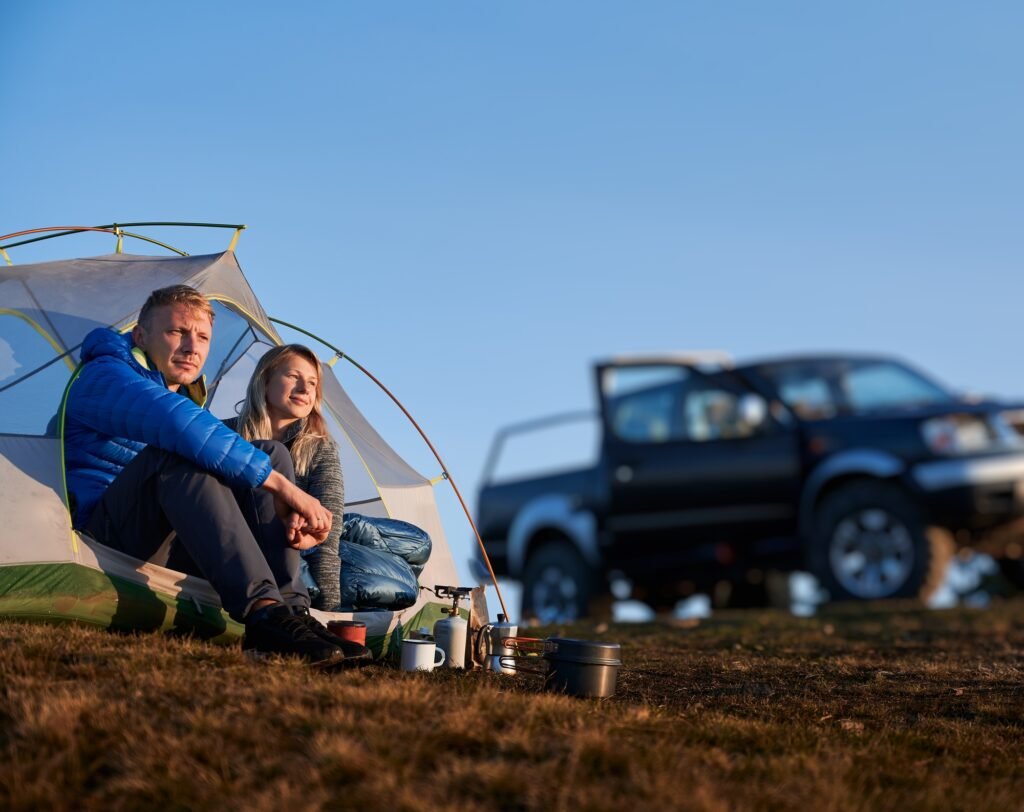 Beautiful young couple sitting in camp tent near car.