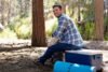 Young man in forest sitting on cool box, Los Angeles, California, USA